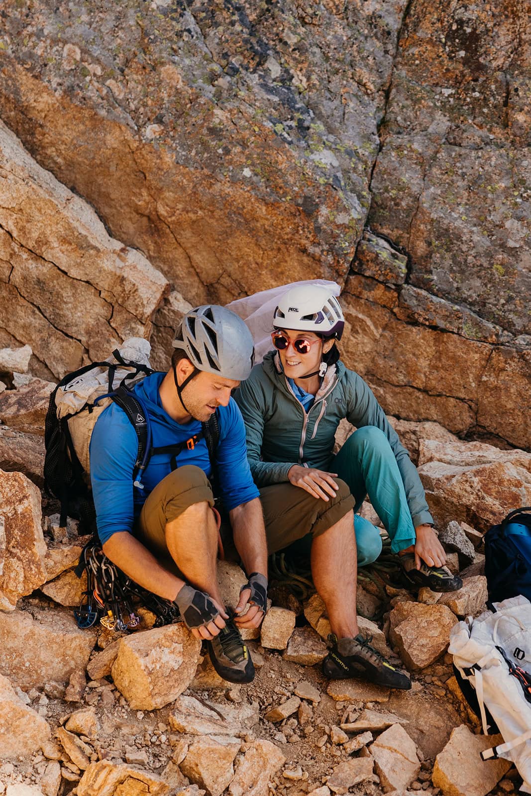 A couple getting their climbing shoes on to begin a climb in the mountains.