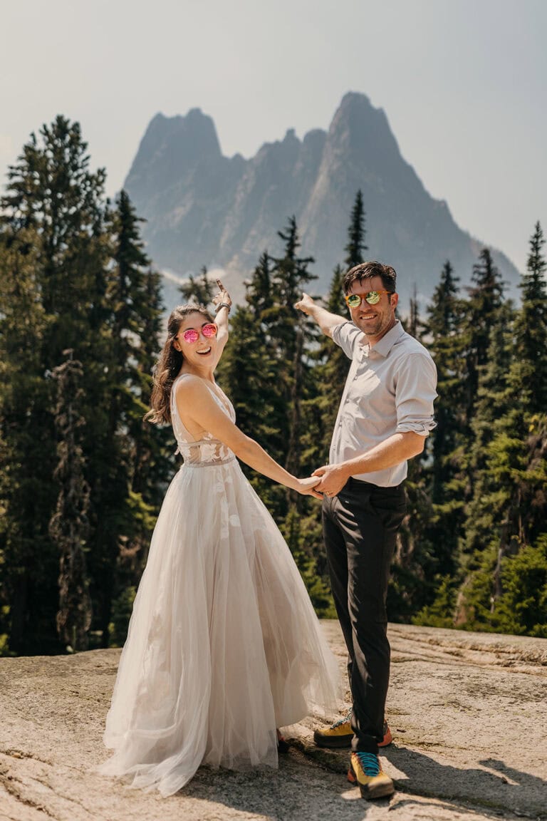 a bride and groom point to liberty bell mountain in the distance.