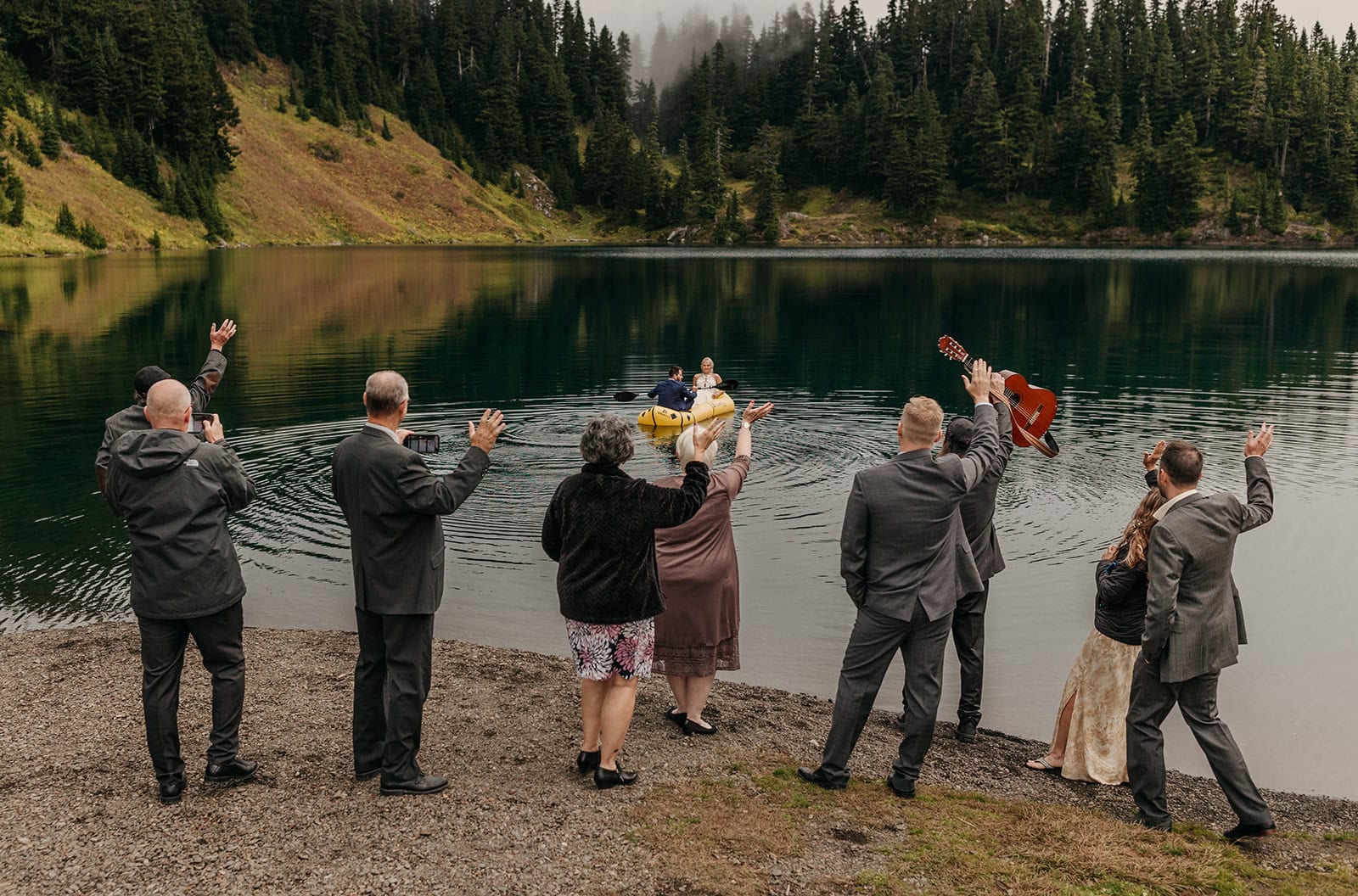 Guest at a couples elopement in Washington wave goodbye to the couple as they float away in a packraft in an alpine lake.