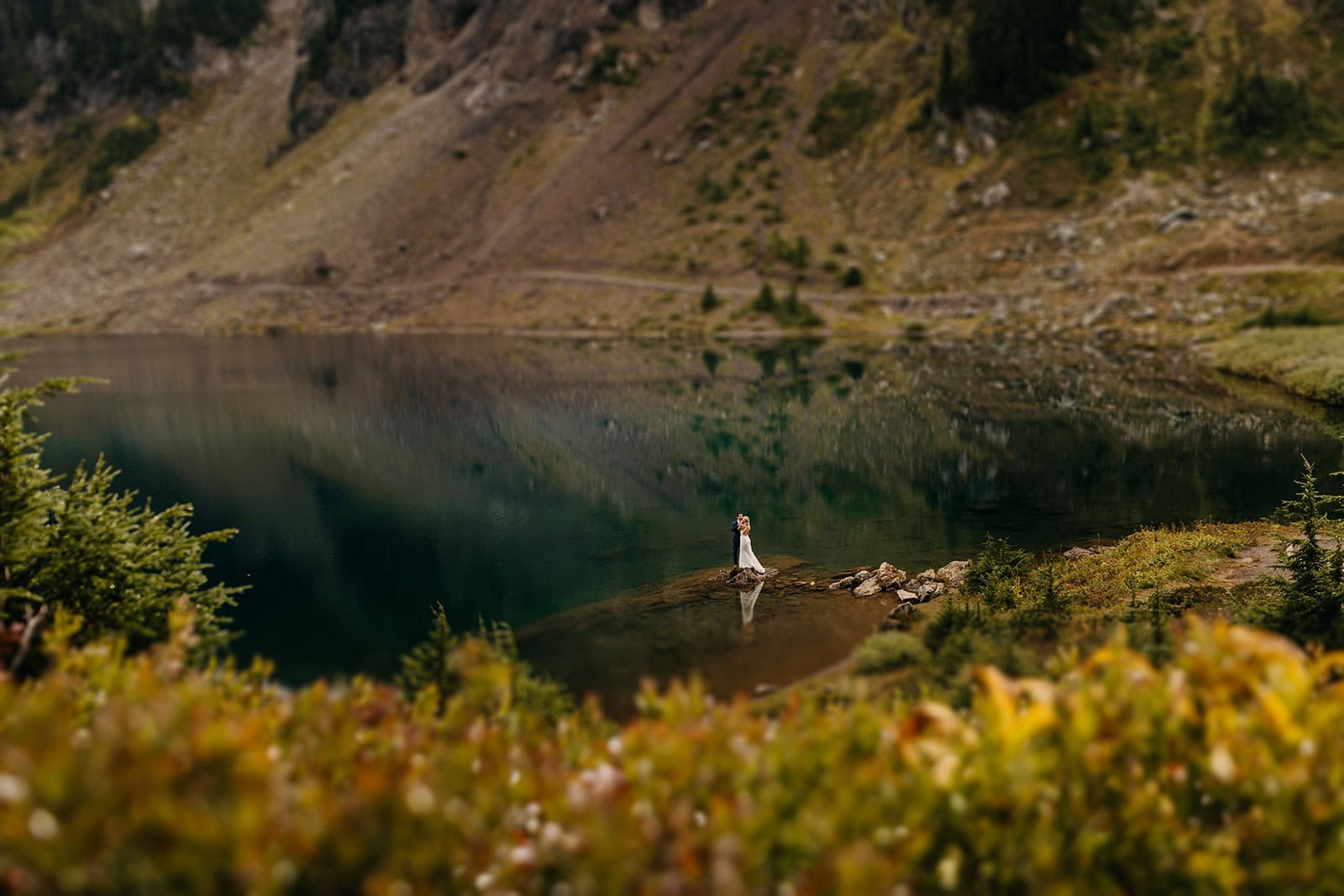 A couple stands by a lake for a portrait on a fall am.