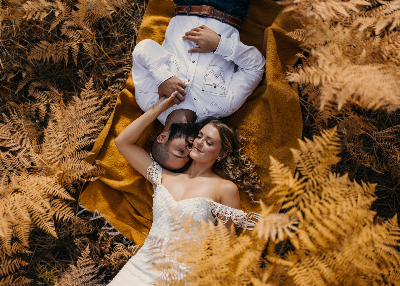 A couple lays among the golden ferns in the high desert on their elopement day.