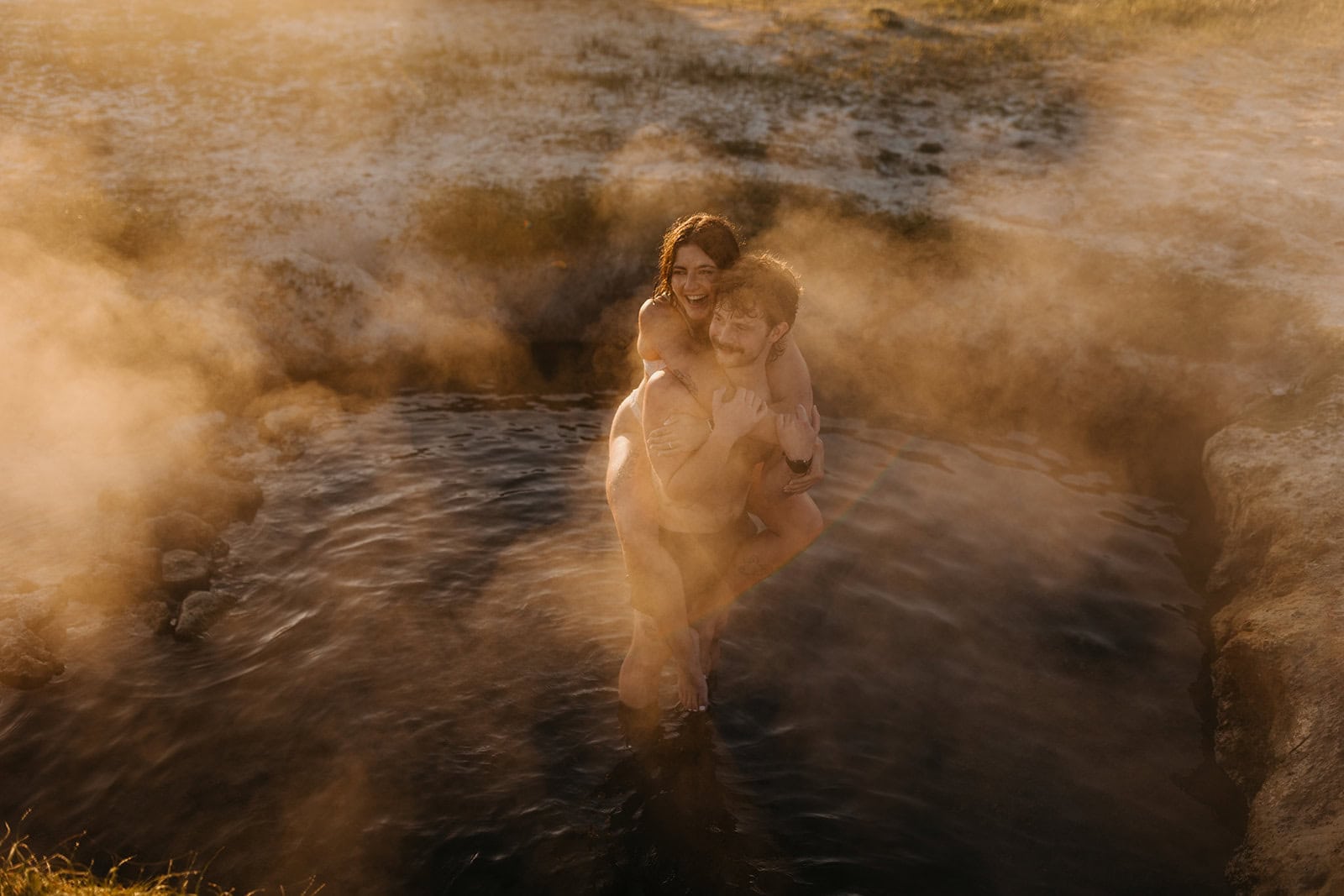 A couple romantically and playfully spend time together in a natural hot spring at sunrise.