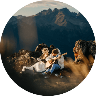 A couple sitting in the mountains smiling while one plays guitar 