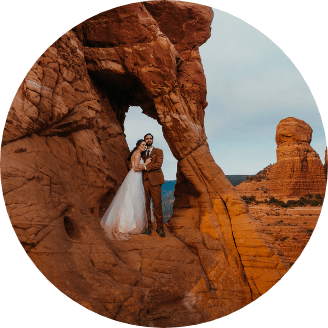 A newlywed couple standing close together in a small arch in red rocks