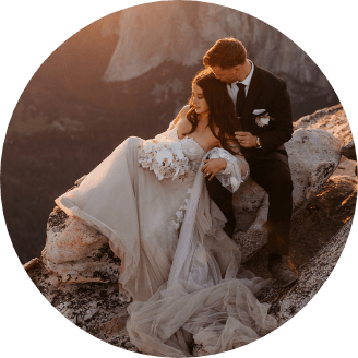 A newlywed couple sitting on a rock together as one leans into the other 