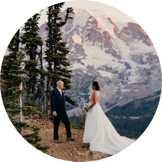 Two marriers hold hands surrounded by snow-capped mountains.